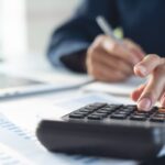 Imagem de uma pessoa com caneta na mão direita e uma calculadora